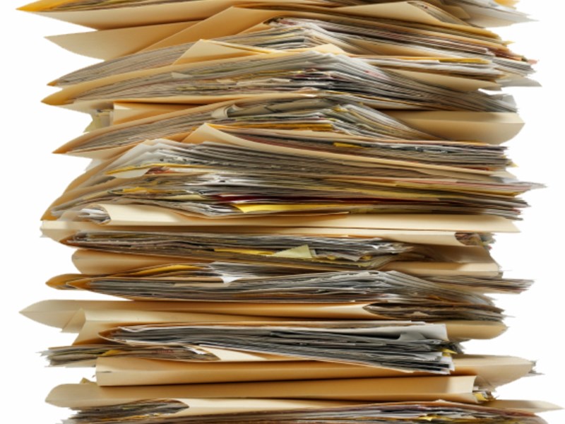 Tall stack of overflowing file folders filled with paper documents