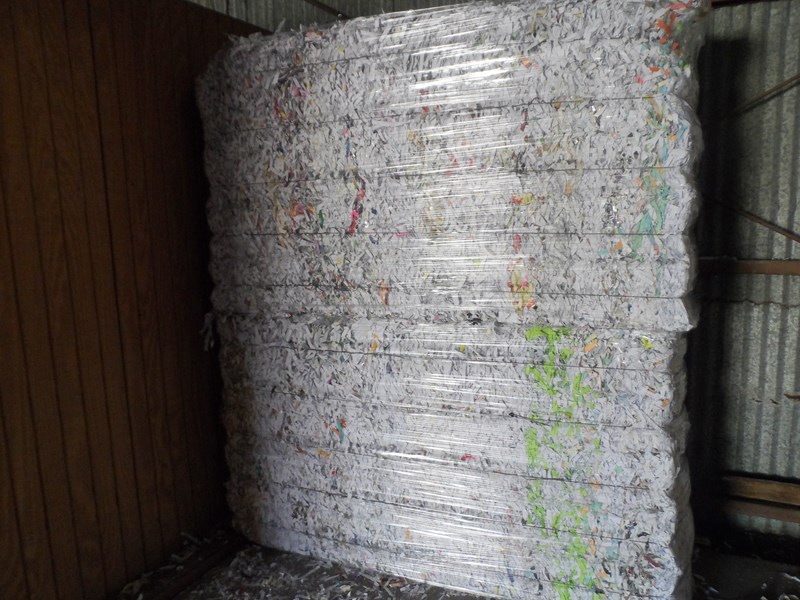Large bale of shredded and recycled paper tightly wrapped in plastic, stored in a warehouse
