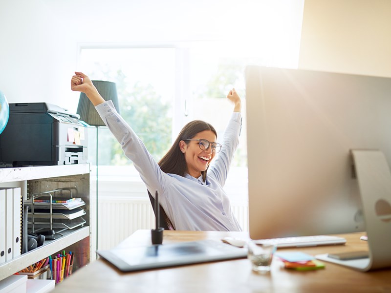Happy woman stretching at her desk in a bright office, feeling accomplished